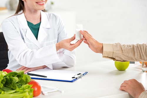 cropped view of dietitian giving pills to patient at workplace