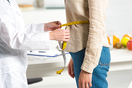 cropped view of dietitian in white coat measuring waist for patient