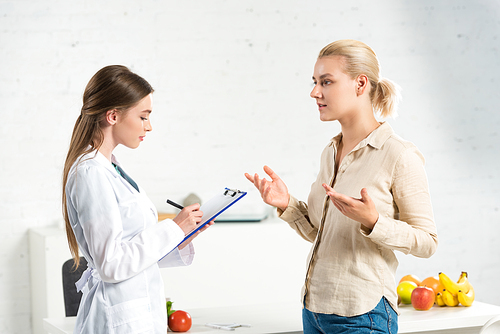 side view of dietitian in white coat writing in clipboard and patient