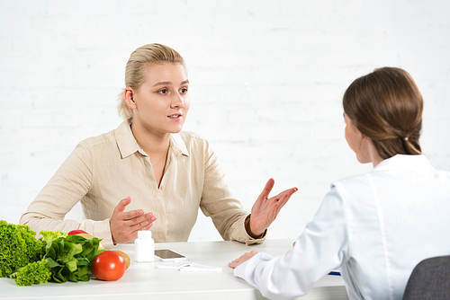 patient and dietitian in white coat at table with fresh vegetables
