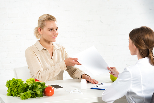 dietitian in white coat giving paper to patient at workplace
