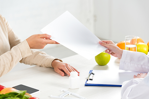cropped view of dietitian giving paper to patient at workplace