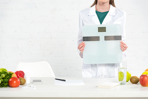 cropped view of dietitian in white coat holding digital scales