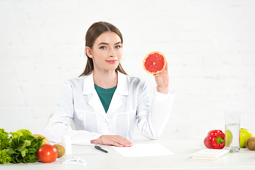 dietitian in white coat holding cut grapefruit at workplace