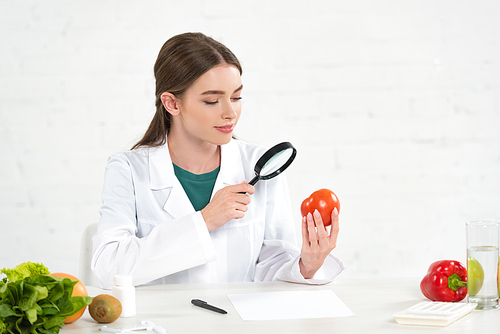 dietitian in white coat looking at tomato through magnifying glass