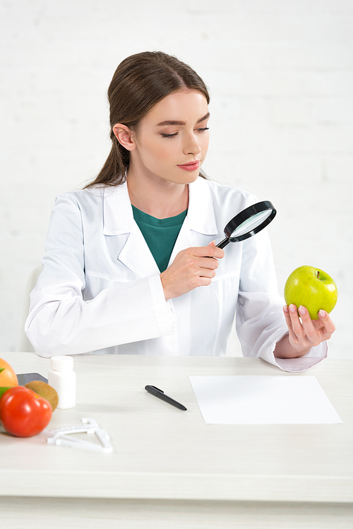 dietitian in white coat looking at apple through magnifying glass