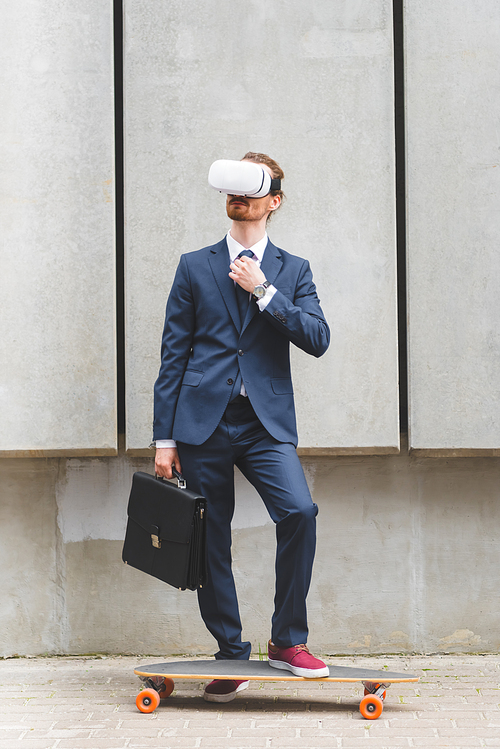 businessman in formal wear and vr headset standing near skateboard with briefcase in hand