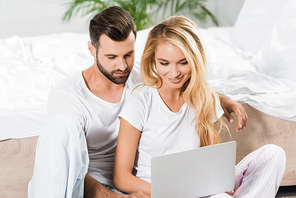beautiful couple using laptop in bed at home