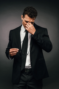tired african american businessman in suit rubbing his eyes on dark background