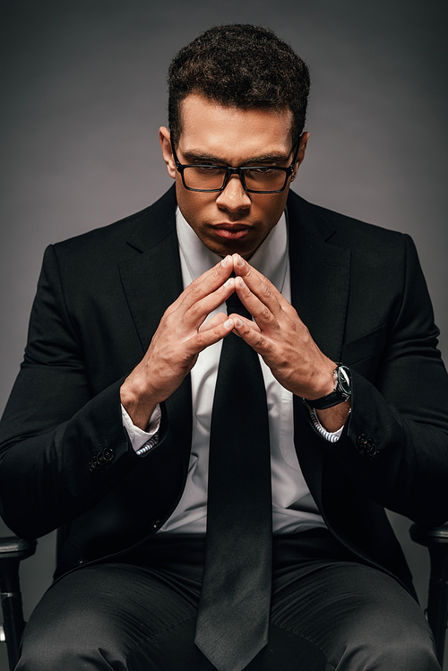 tense african american businessman in suit and glasses on dark background