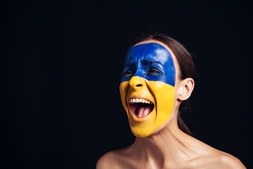 emotional naked young woman with painted Ukrainian flag on face screaming isolated on black