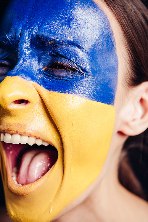 close up view of young woman with painted Ukrainian flag on skin screaming and crying isolated on black