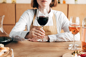 cropped view of sommelier in apron holding wine glass while sitting at table