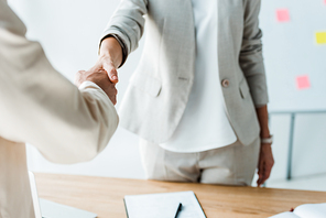 cropped view of recruiter and employee shaking hands while standing  in office