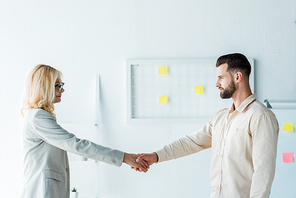 attractive recruiter in glasses and handsome employee shaking hands