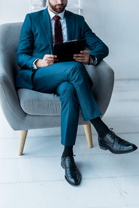 cropped view of bearded man sitting in crossed legs and holding clipboard
