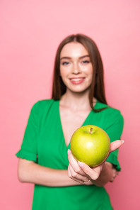 selective focus of attractive young woman holding green apple and smiling isolated on pink