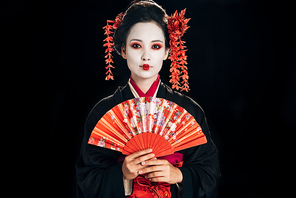 beautiful geisha in black kimono with red flowers in hair holding traditional hand fan isolated on black