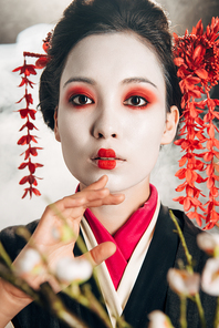 portrait of beautiful geisha in black kimono with red flowers in hair and sakura branches on black background with smoke