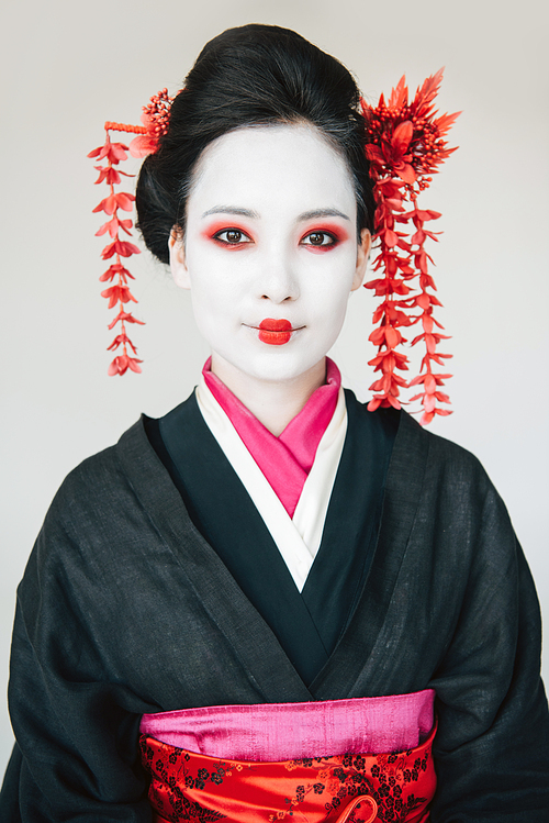 smiling beautiful geisha in black kimono with red flowers in hair isolated on white