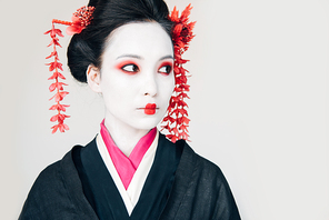 beautiful geisha in black kimono with red flowers in hair looking away isolated on white