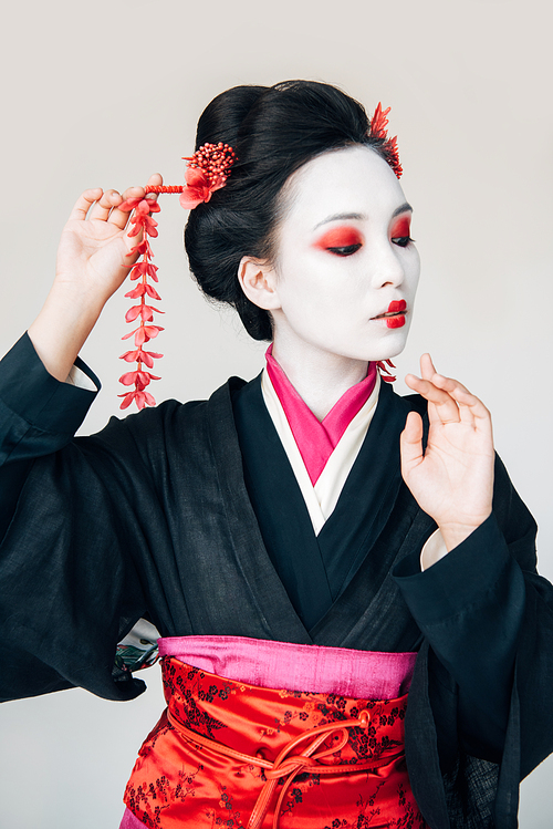 beautiful geisha in black kimono with red flowers in hair gesturing isolated on white