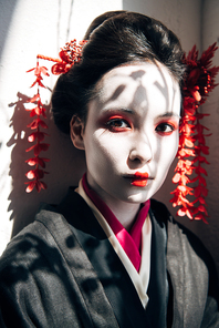 portrait of beautiful geisha with red and white makeup  in sunlight with shadows