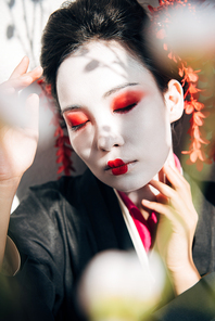 selective focus of tree branches and beautiful geisha with red and white makeup in sunlight