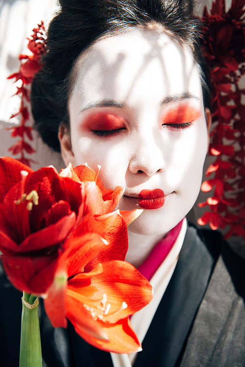 portrait of beautiful geisha holding red flowers in sunlight
