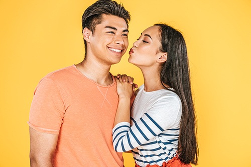 beautiful asian girl kissing happy boyfriend isolated on yellow
