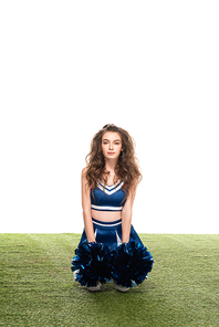 cheerleader girl in blue uniform with pompoms sitting on green field isolated on white