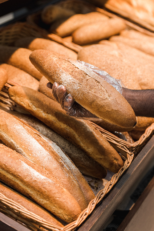 cropped view of african american man holding baguette in supermarket