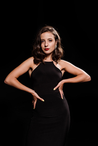 elegant young woman standing with hands on hips isolated on black