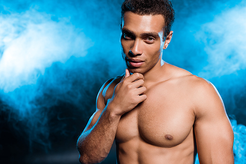 sexy mixed race man touching face on blue with smoke