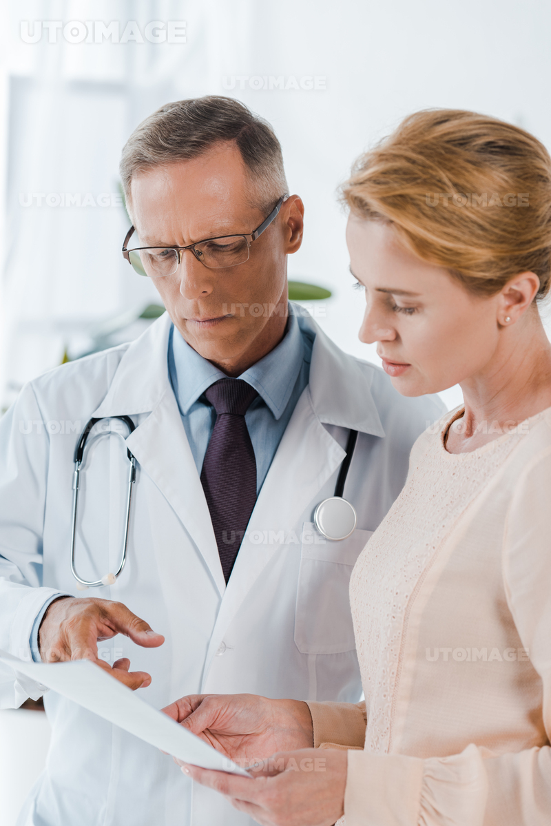 유토이미지 | doctor in glasses pointing with finger at document near woman