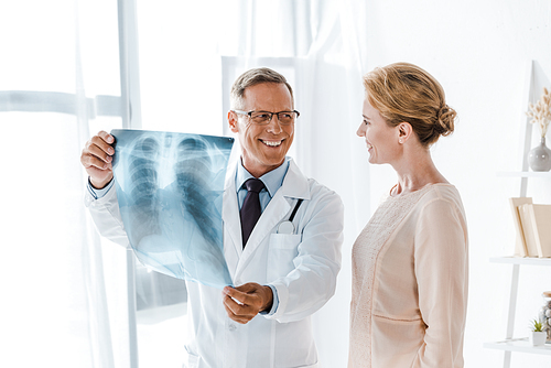 happy doctor looking at attractive patient and holding  x-ray in clinic