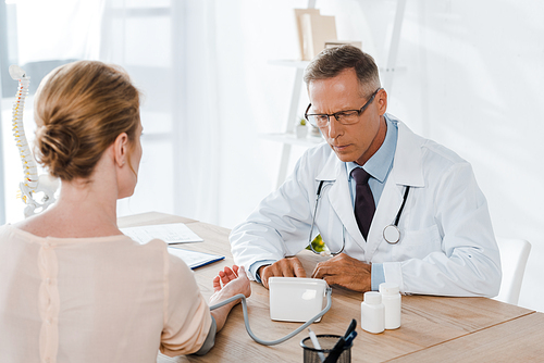 selective focus of doctor in glasses measuring blood pressure of woman