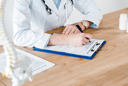 cropped view of doctor writing diagnosis on wooden table