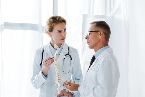 attractive doctor holding spine model near coworker in glasses