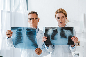doctor in glasses and attractive coworker looking at x-rays in clinic
