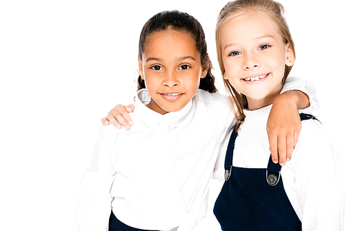two happy multicultural schoolgirls hugging and smiling at camera isolated on white