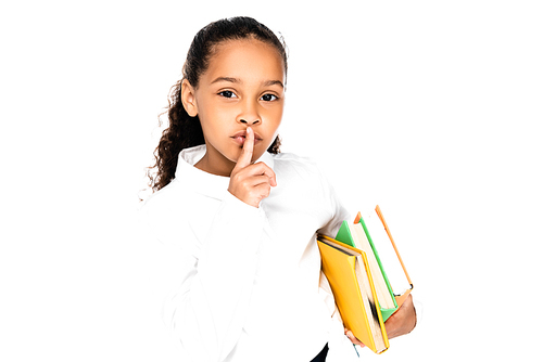 adorable african american schoolgirl holding books and showing hush gesture isolated on white