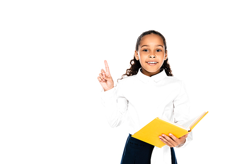 cheerful african american schoolgirl holding book and showing idea gesture isolated on white