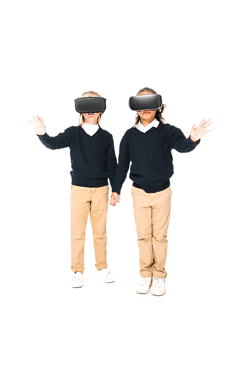 full length view of two multicultural schoolgirls holding hands while using virtial reality headsets on white background