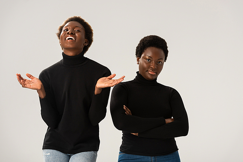 laughing african american girls in black turtlenecks with crossed arms isolated on grey