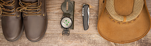 panoramic shot of boots, compass, jackknife and hat on wooden table