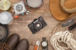 top view of photo camera, hat, boots and hiking equipment on wooden table