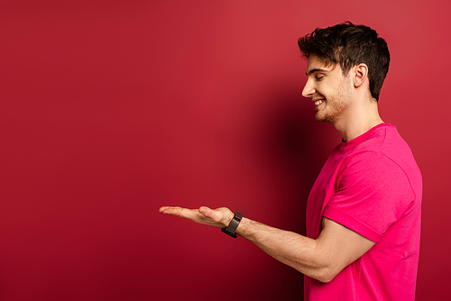 portrait of smiling man in pink t-shirt presenting something on red