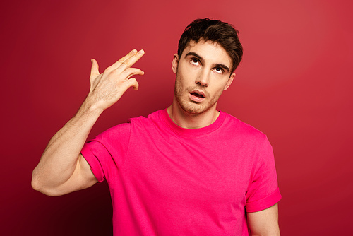 portrait of frustrated man in pink t-shirt with hand gun gesture on red