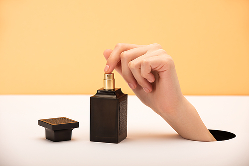 cropped view of woman touching perfume bottle on orange and white